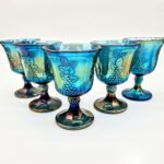 Set of five blue carnival glass goblets with iridescent finish and embossed grapevine pattern.