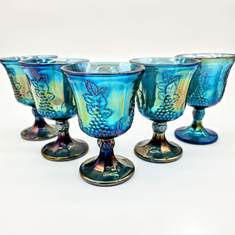 Set of five blue carnival glass goblets with iridescent finish and embossed grapevine pattern.