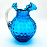 Fenton blue hobnail glass pitcher with ruffled rim and clear ribbed handle.