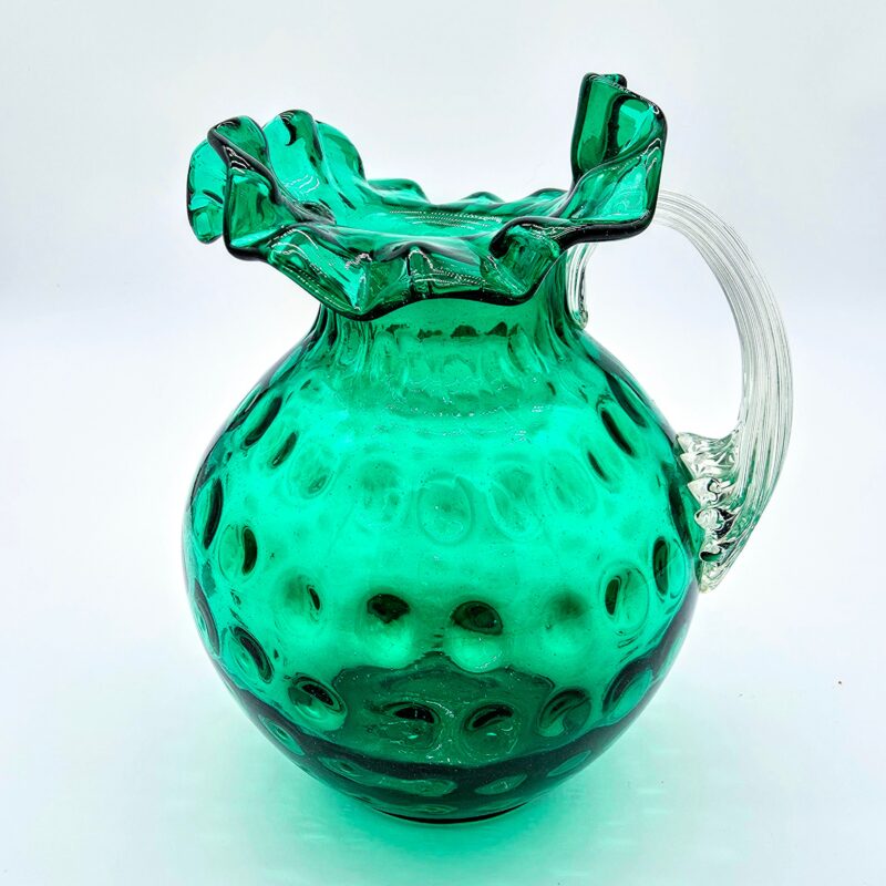 Fenton green hobnail glass pitcher with ruffled rim and clear ribbed handle.