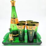 Green and gold Oriental-style glass decanter set with tray, glasses, and bell featuring floral enamel design.