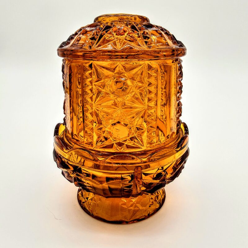 Vintage amber-orange pressed glass fairy light with starburst pattern and pedestal base.