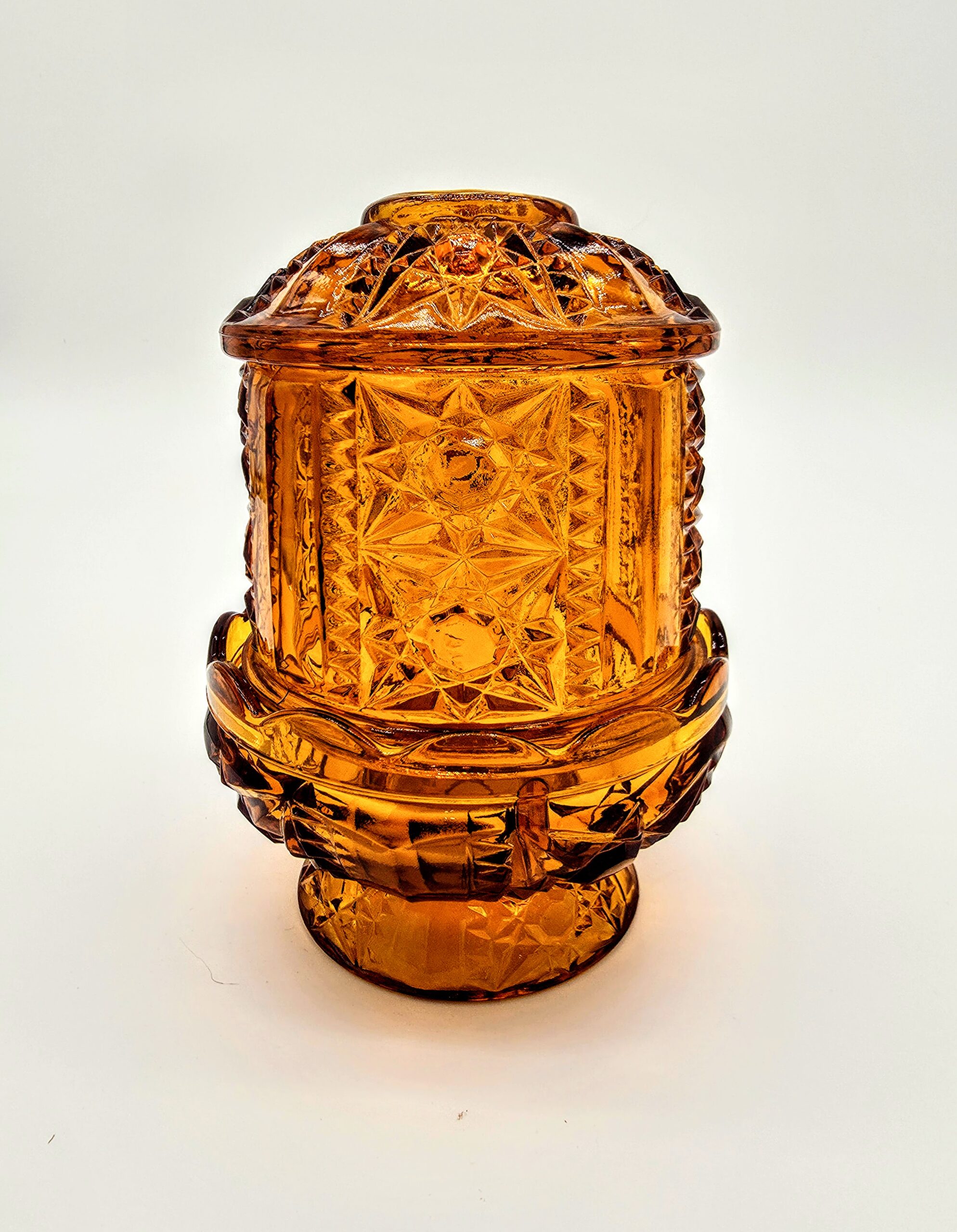 Vintage amber-orange pressed glass fairy light with starburst pattern and pedestal base.
