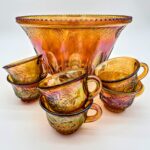 Orange carnival glass punch bowl and six matching cups with iridescent grape and vine design.