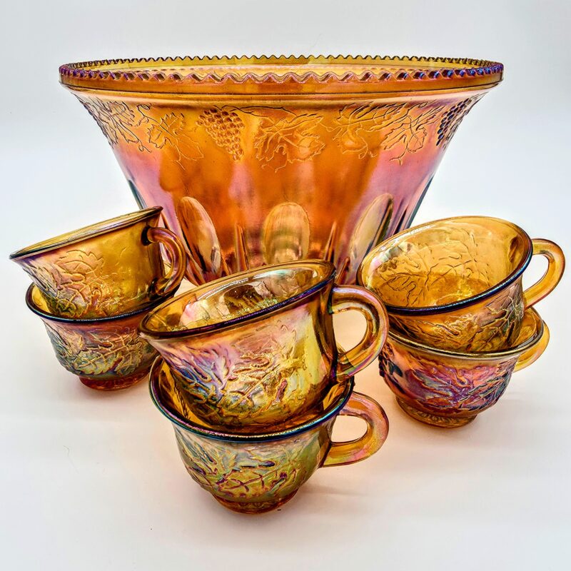 Orange carnival glass punch bowl and six matching cups with iridescent grape and vine design.