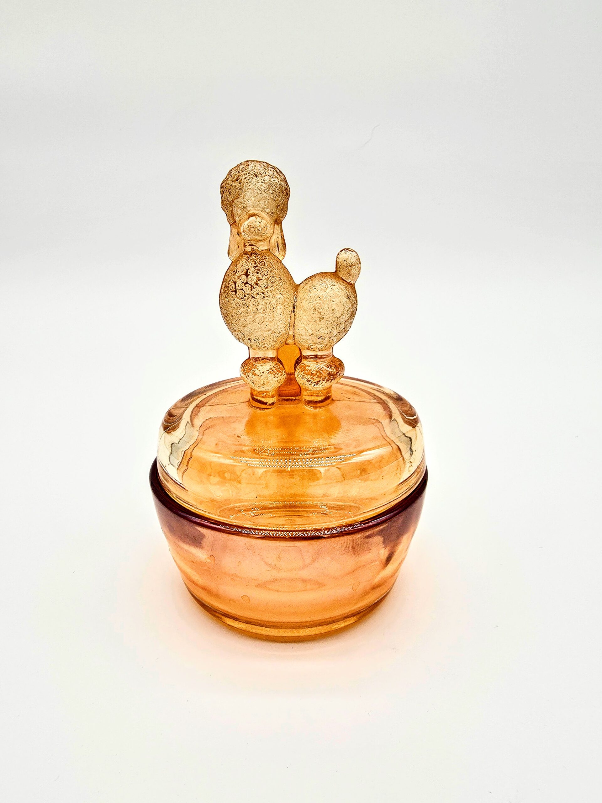 Vintage orange pressed glass candy dish with poodle-shaped lid and iridescent amber tone.