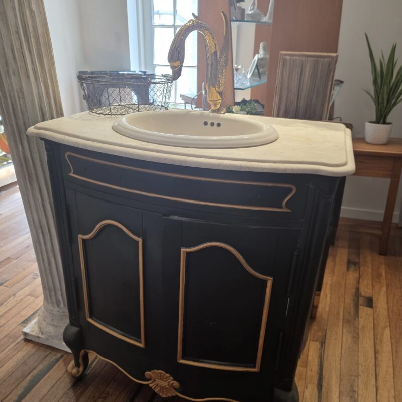 French Provincial black and gold vanity with white marble top and brass swan faucet, vintage European-style bathroom furniture.